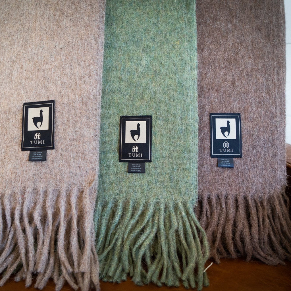 Tan, green and brown alpaca wool blend throws hanging side by side, showing brushed texture and fringe
