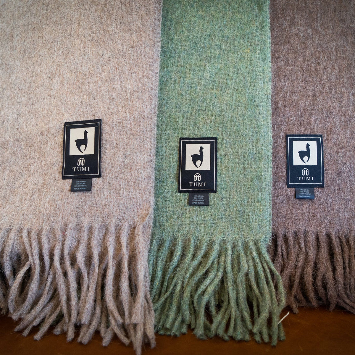 Tan, green and brown alpaca wool blend throws draped together over the back of a leather chair