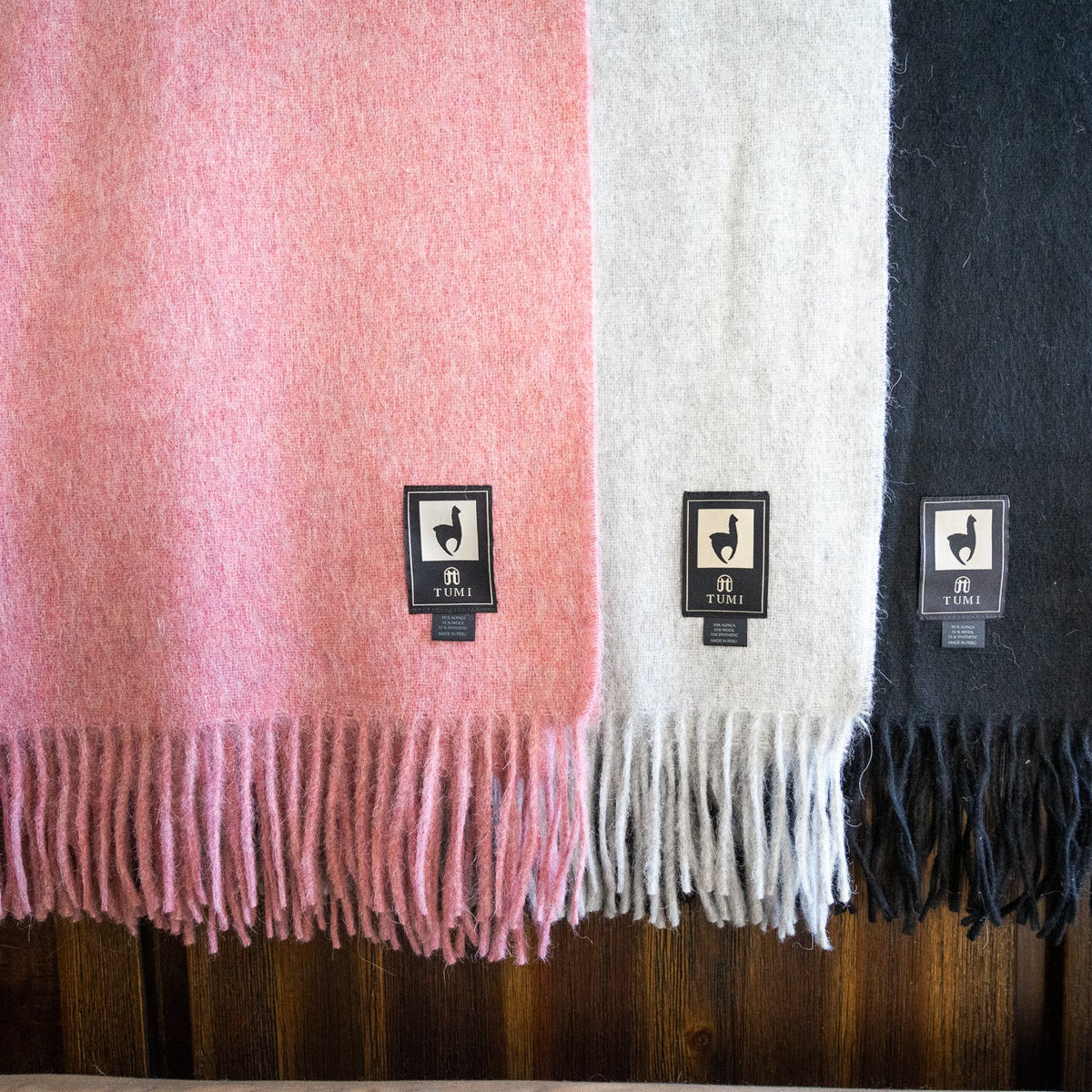 Pink, cream and black alpaca wool blend throws hanging over a dark wood rail with fringe at the hem