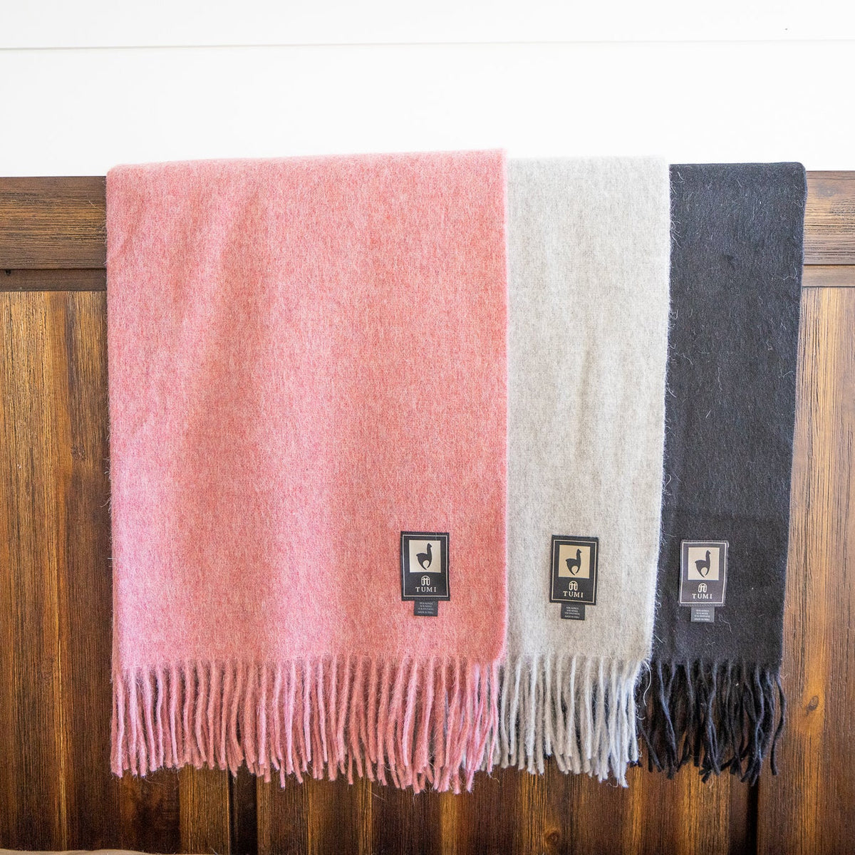Pink, cream and black alpaca wool blend throws hanging in a row on a dark wood rail, wide view