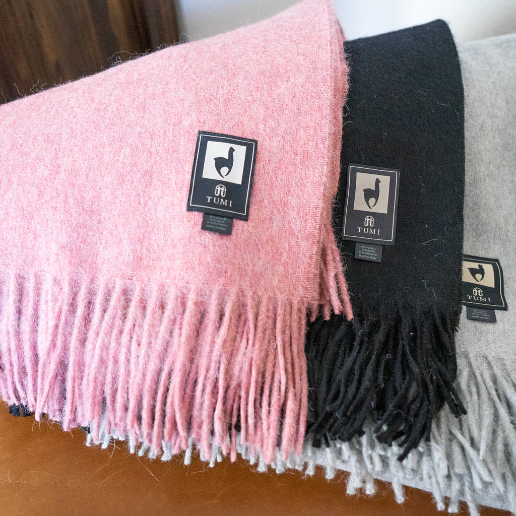 Pink, black and light gray alpaca wool blend throws with fringe layered over a leather chair arm