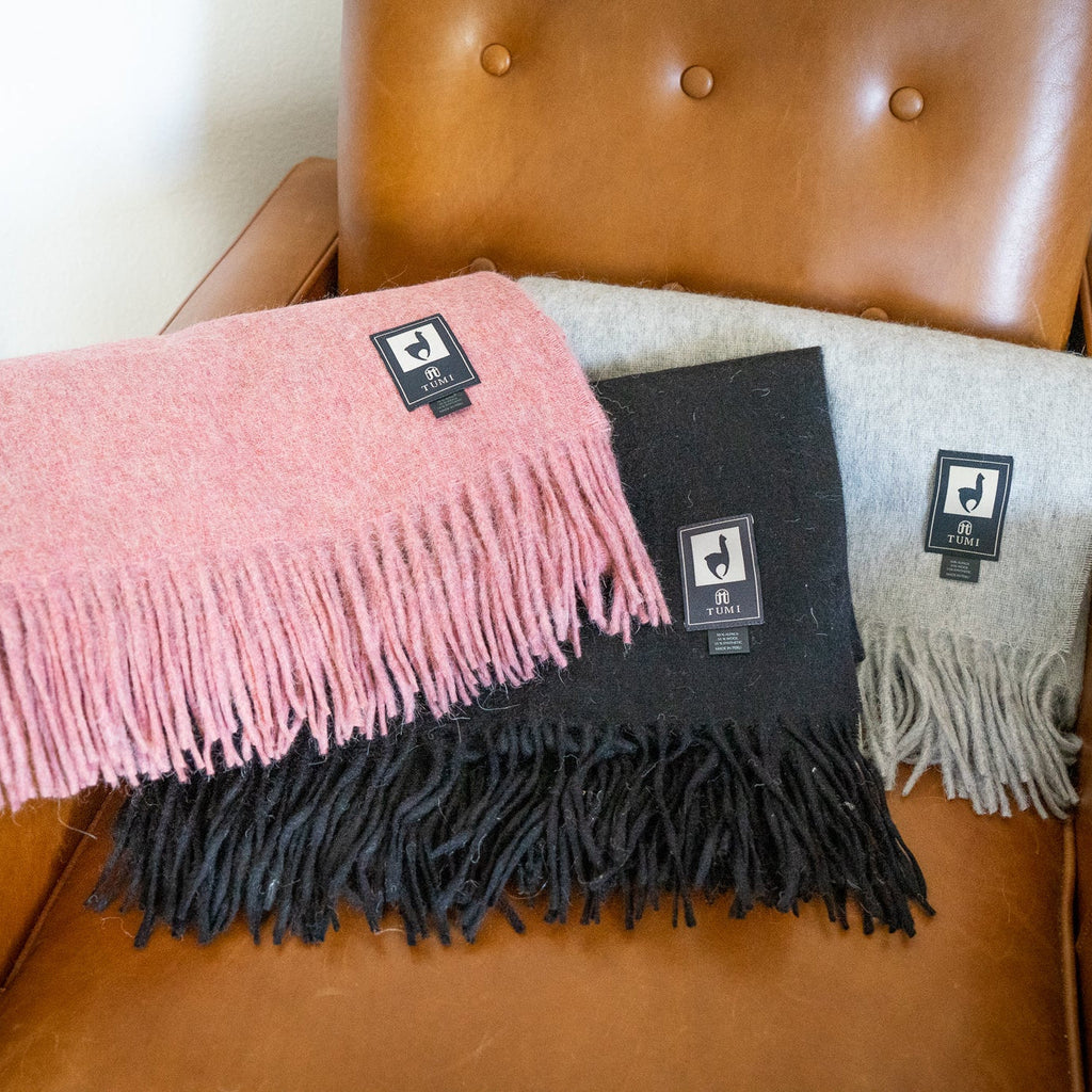 Pink, black and light gray alpaca wool blend throws folded and stacked on a tan leather armchair