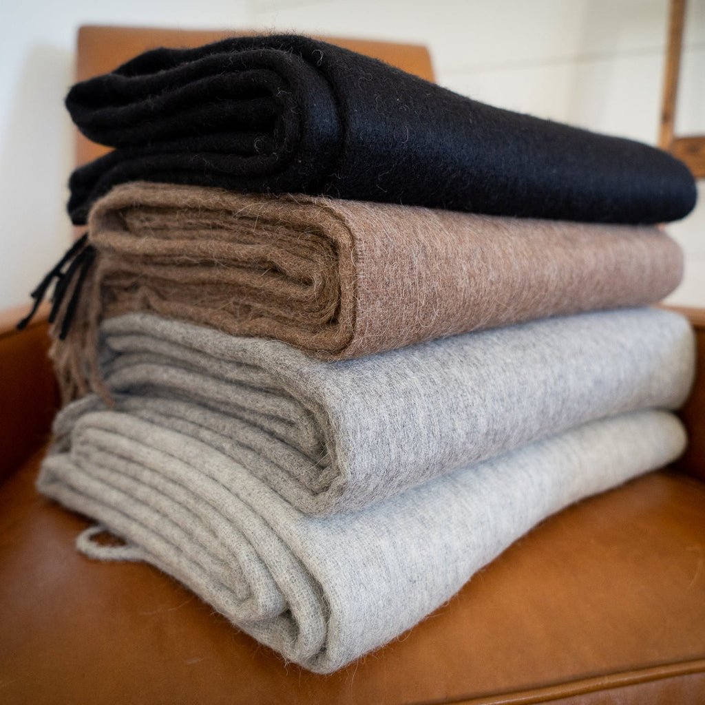 Stack of folded alpaca wool blend throws in black, brown, gray and cream on a tan leather chair