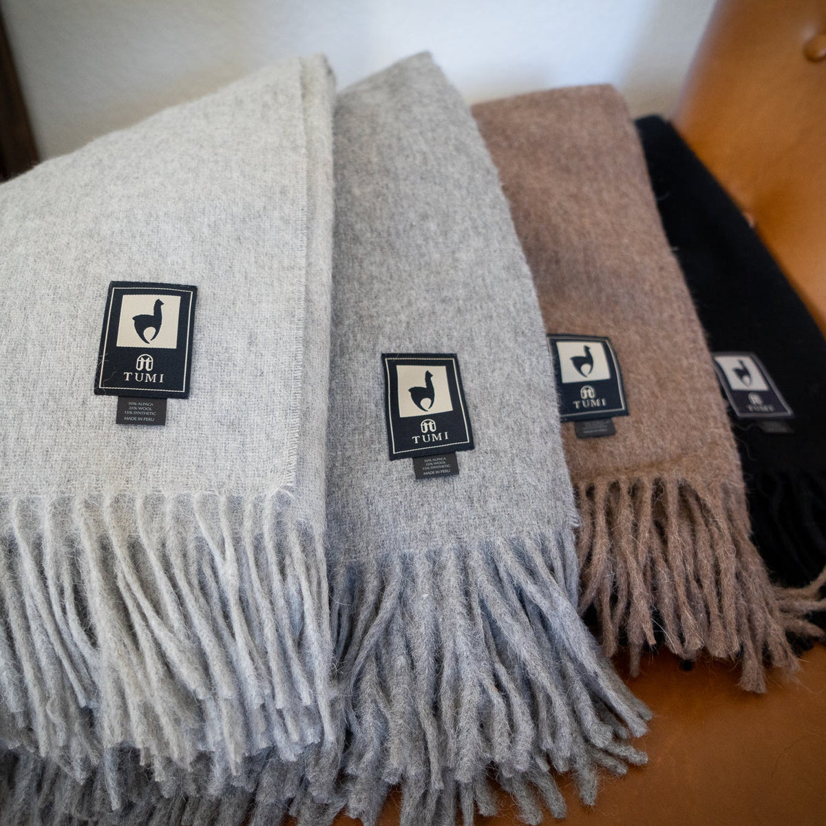 Four alpaca wool blend throws in cream, gray, brown and black fanned across a tan leather chair