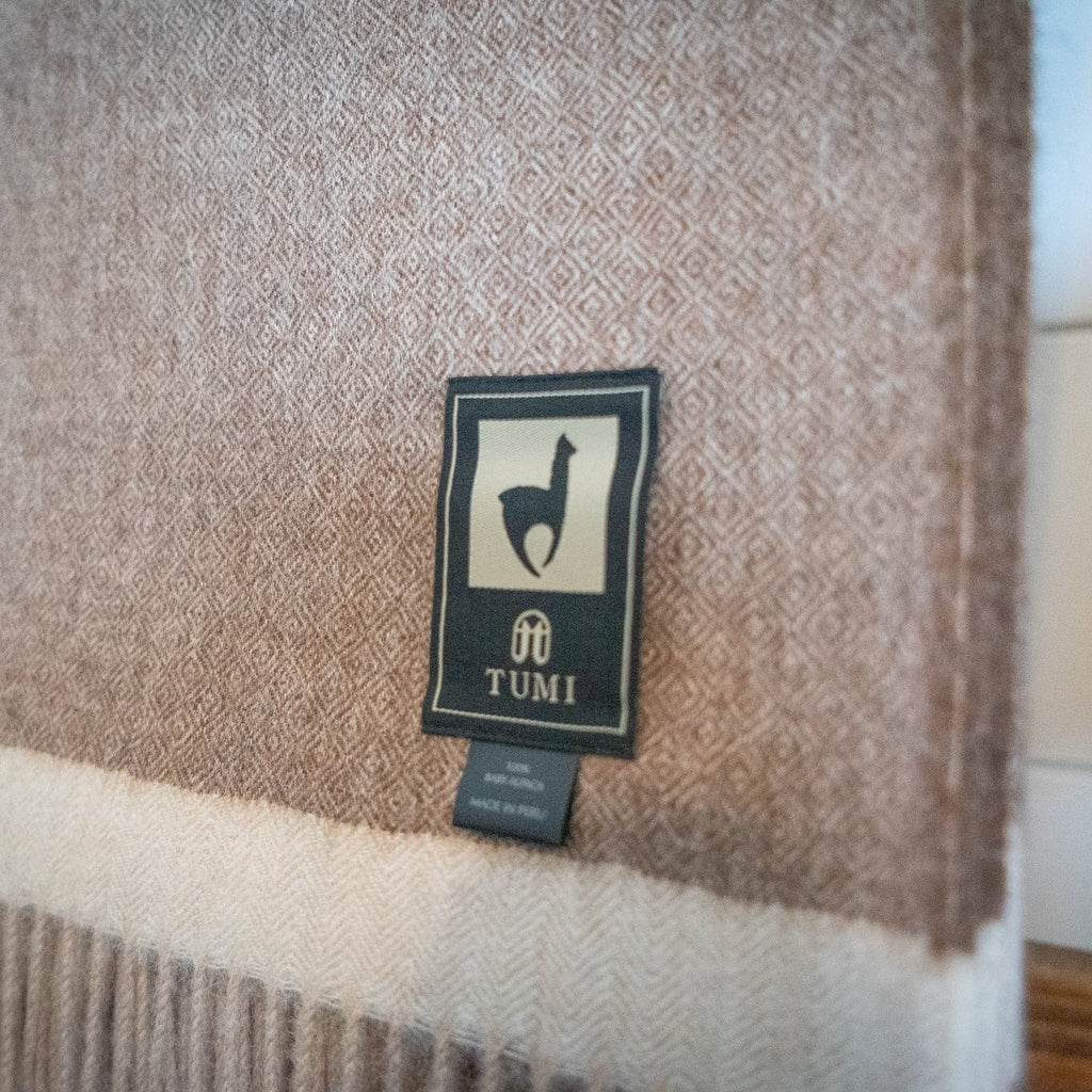 Detail of brown baby alpaca herringbone weave above a cream band, seen on a wooden blanket ladder