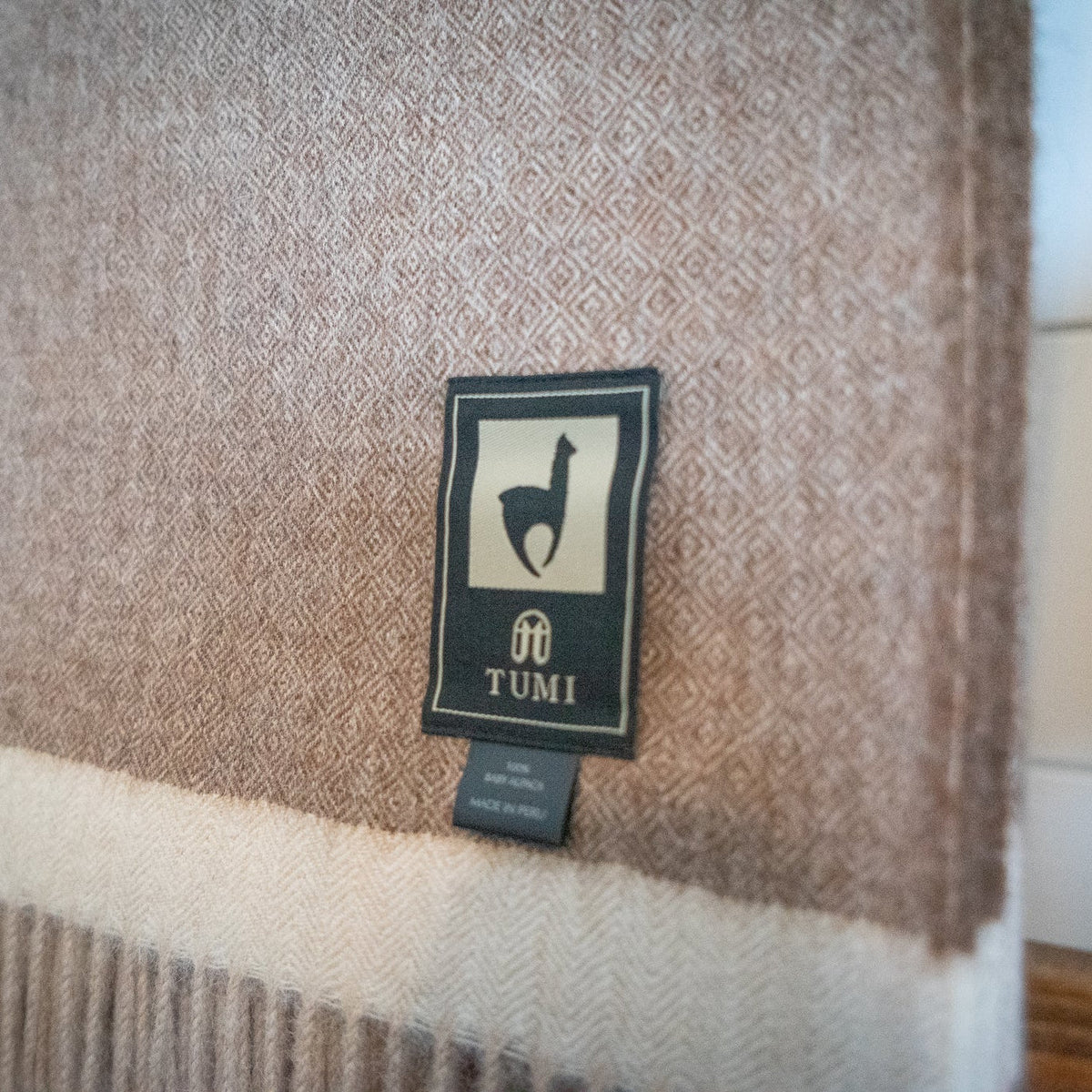 Detail of brown baby alpaca herringbone weave above a cream band, seen on a wooden blanket ladder