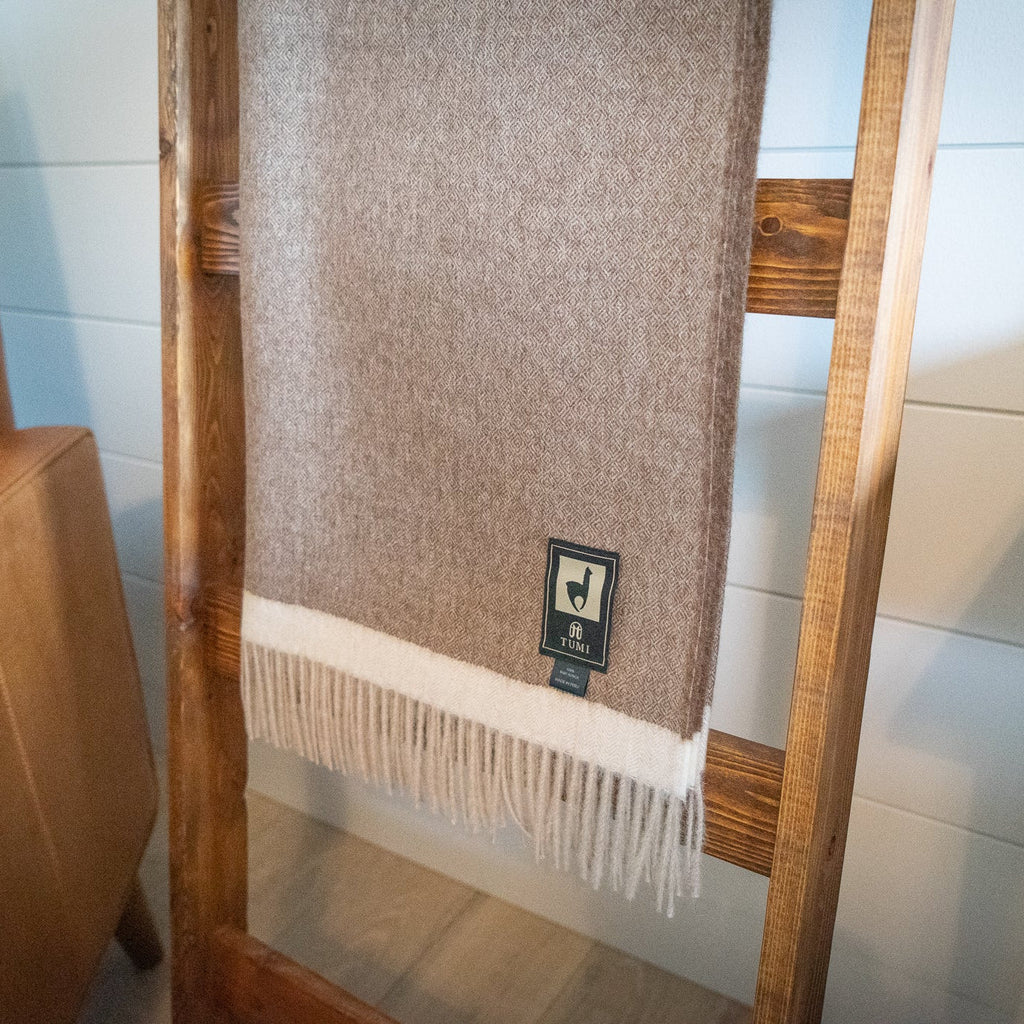 Fringed end of brown baby alpaca herringbone throw with cream band hanging between ladder rungs