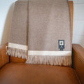 Brown baby alpaca herringbone throw draped in two layers over the back of a tan leather armchair