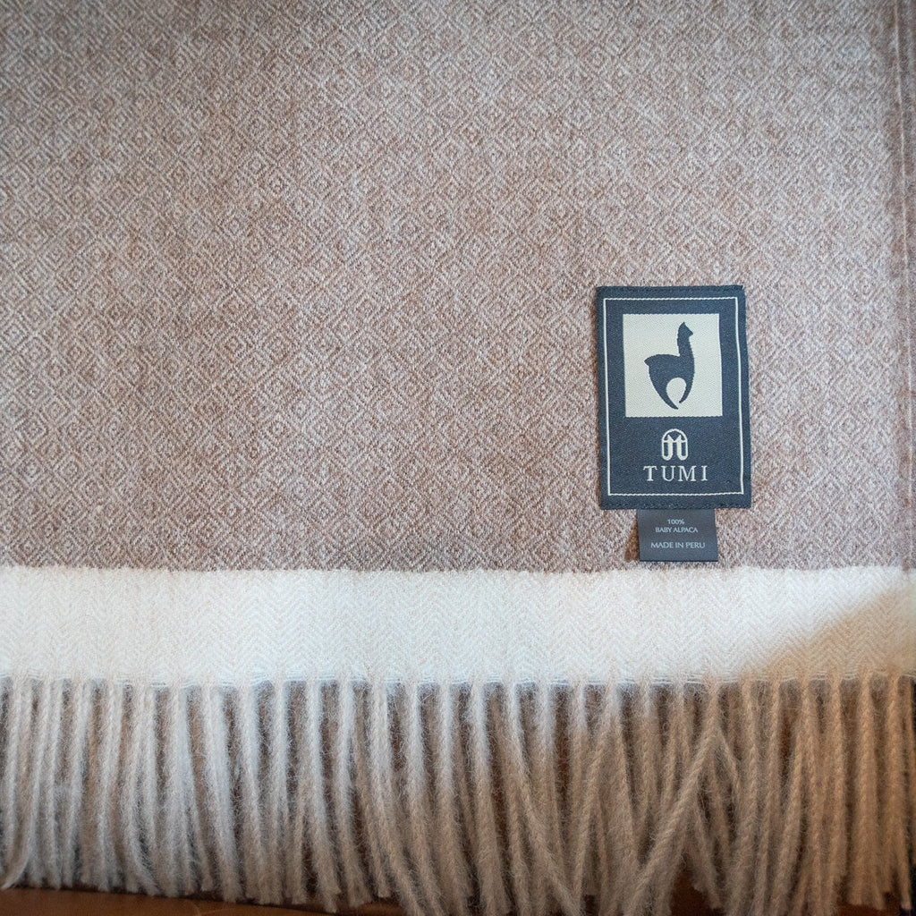 Brown baby alpaca herringbone throw with cream band and fringe draped over a leather chair arm