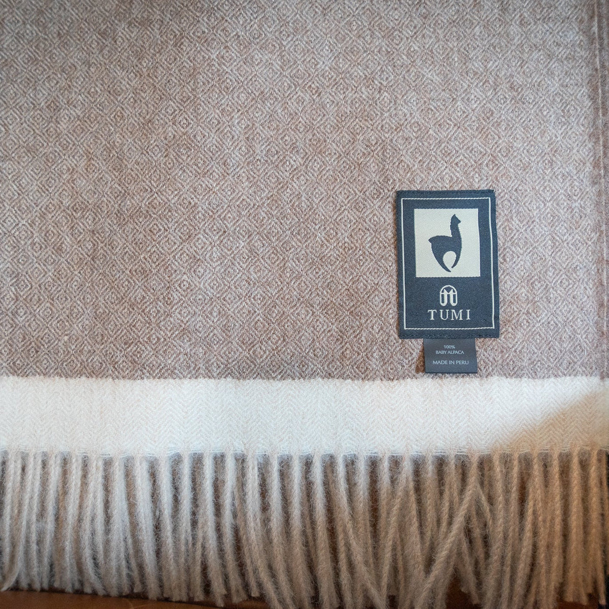 Brown baby alpaca herringbone throw with cream band and fringe draped over a leather chair arm