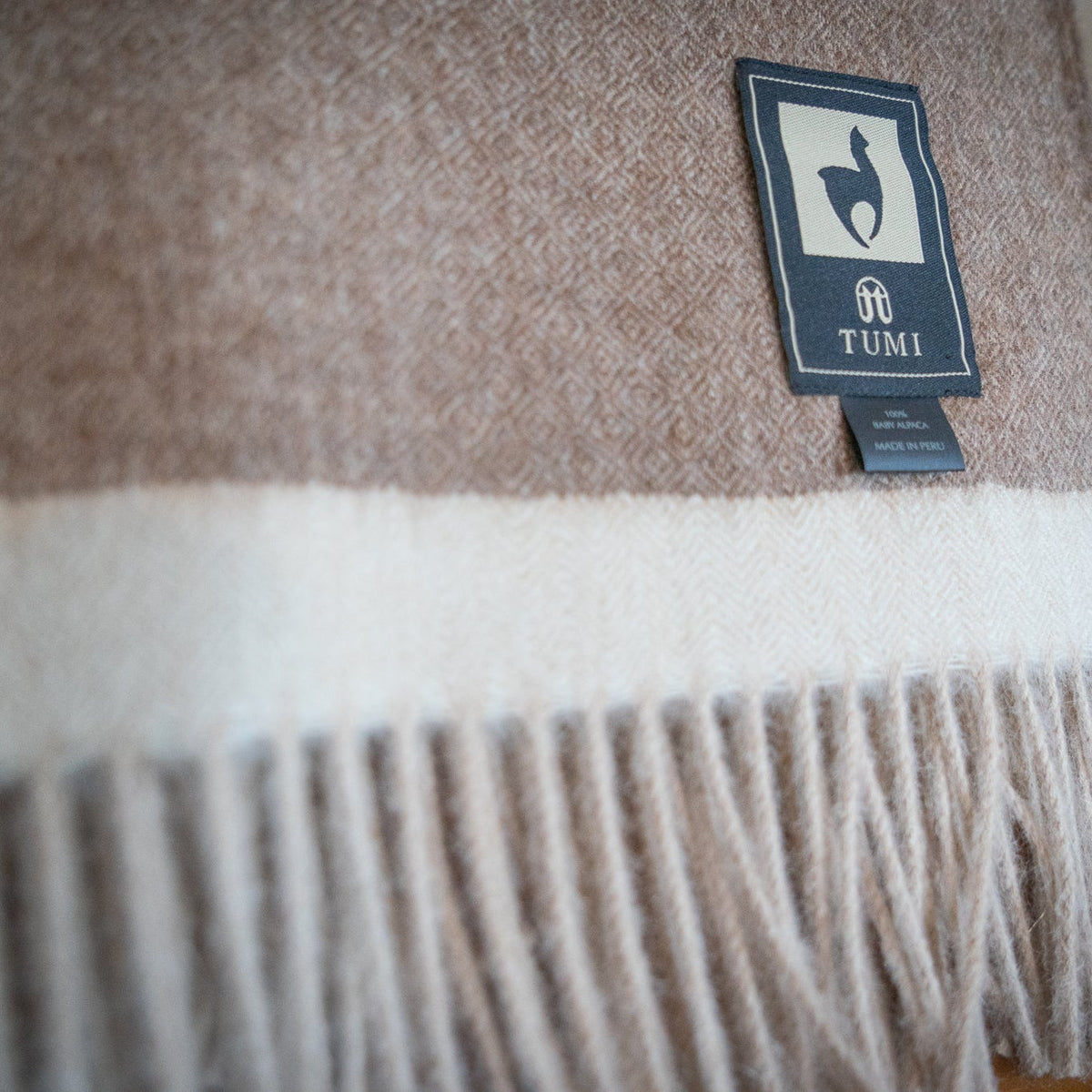 Macro view of the cream band and natural fringe on a brown baby alpaca herringbone throw