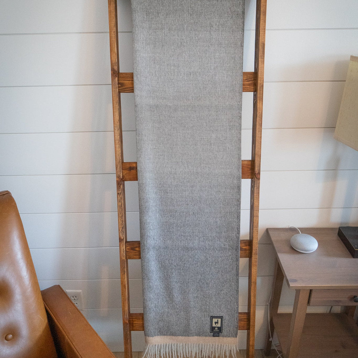 Gray baby alpaca herringbone throw hanging full length on a wooden ladder against a white paneled wall