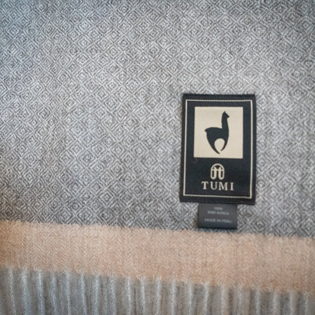 Close view of gray herringbone baby alpaca weave with a soft tan band just above the fringe