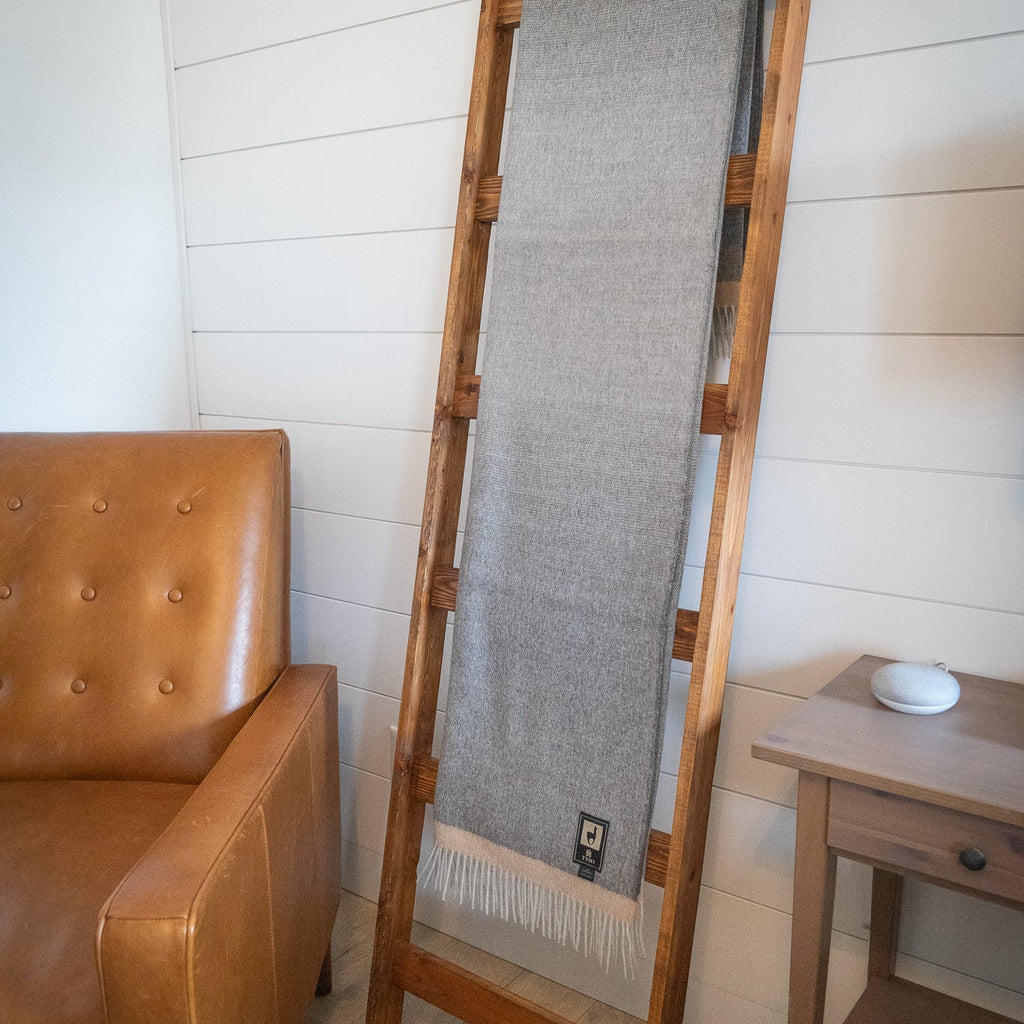 Gray baby alpaca throw on a leaning wooden ladder in a white paneled room beside a tufted leather chair