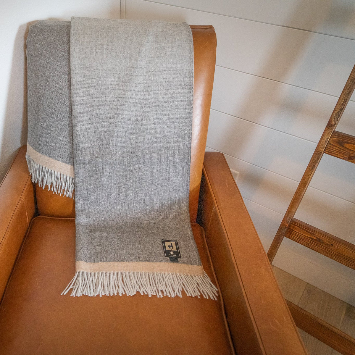 Gray baby alpaca herringbone throw folded lengthwise over the back of a tan leather armchair