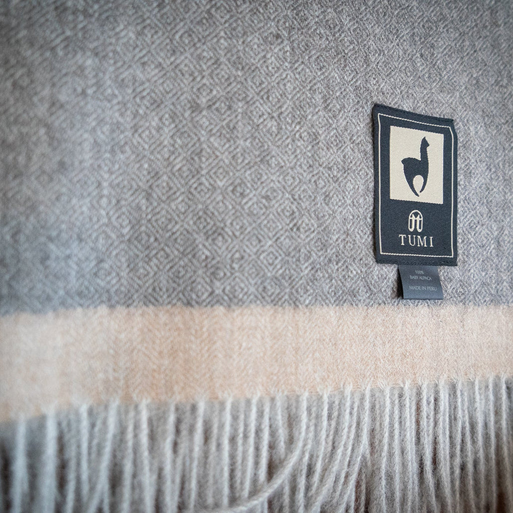Detail of gray baby alpaca herringbone weave with soft tan band and gray fringe on a wooden ladder