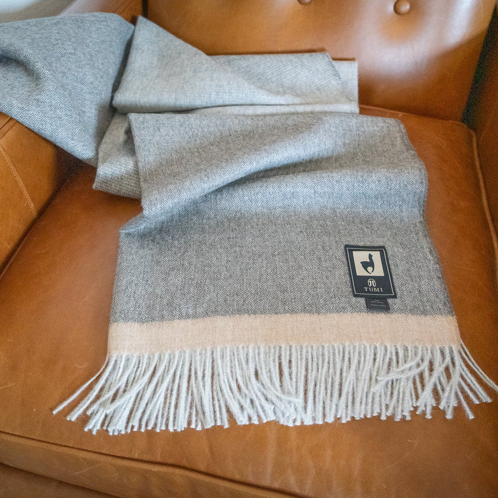 Gray baby alpaca herringbone throw with tan band tossed loosely across a tan leather armchair seat