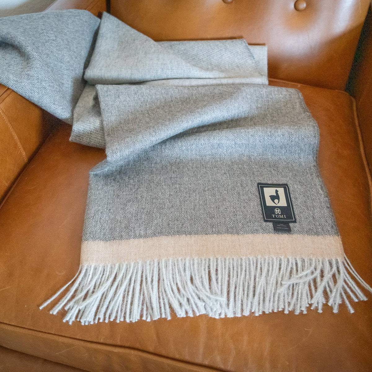 Gray baby alpaca herringbone throw with tan band tossed loosely across a tan leather armchair seat