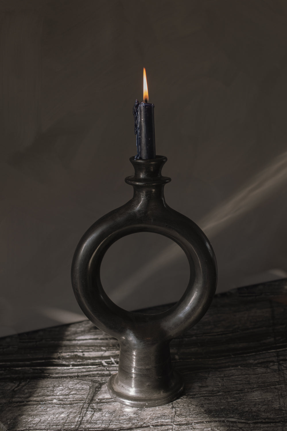 Black ring-shaped terracotta candle holder with a lit taper glowing in a dark room