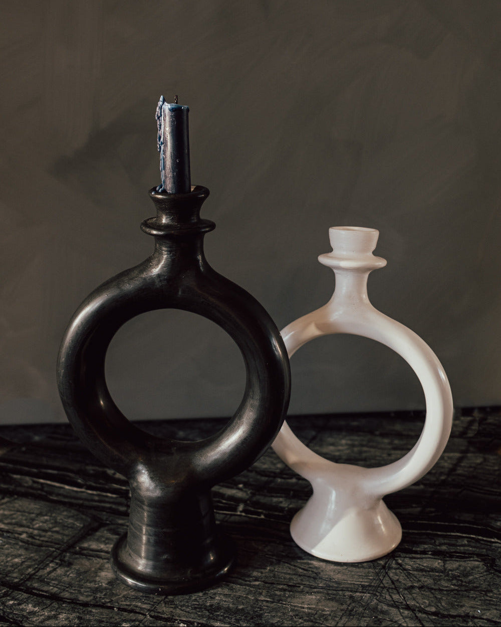 Pair of sculptural glazed terracotta candle holders, one black and one white, on a dark wood table