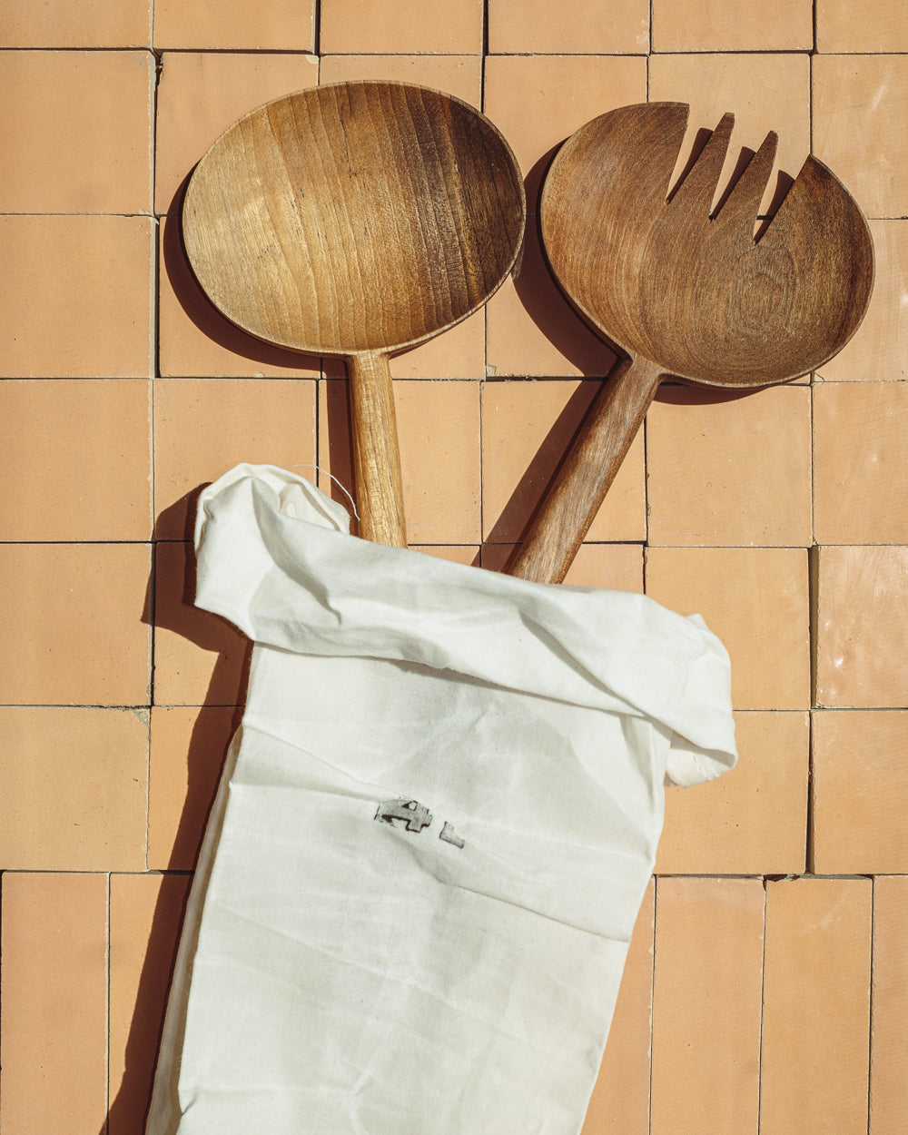 Pair of carved walnut salad servers tucked into a natural linen pouch on warm terracotta tiles
