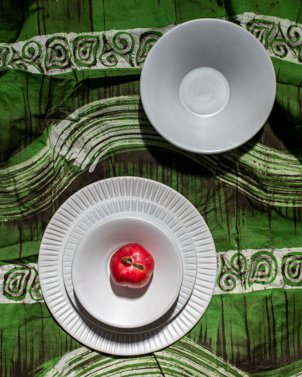 Matte white dinner plate and bowl on a green and white printed cloth, a single red apple at the center