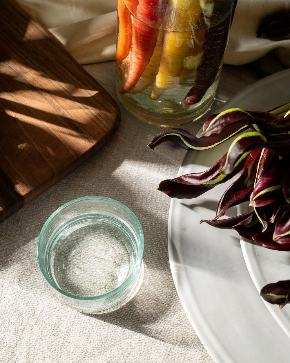 Small recycled glass tumbler of water seen from above on linen beside a plate and a wood board