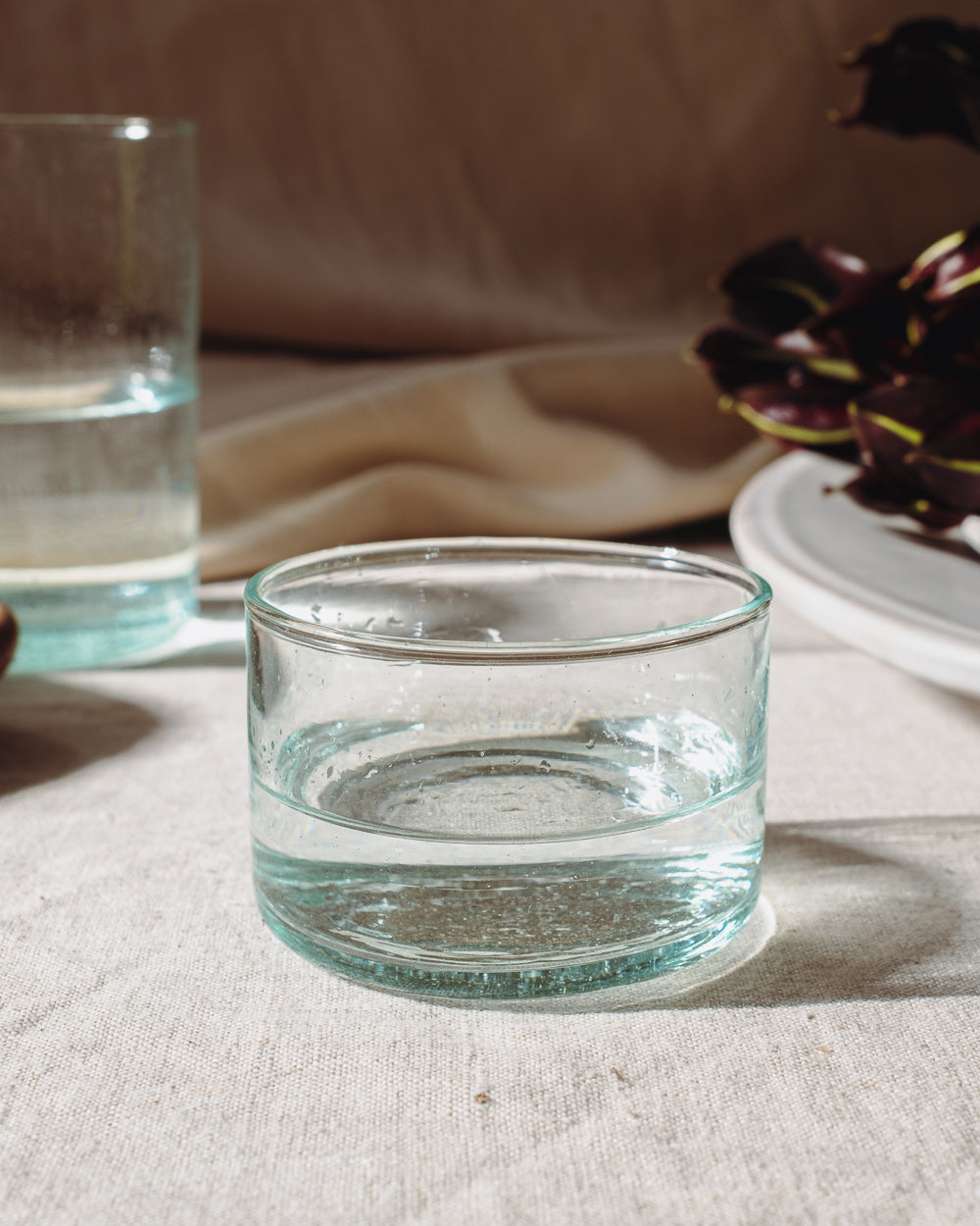 Short wide recycled glass tumbler on a linen cloth, showing the faint green tint of the recycled glass