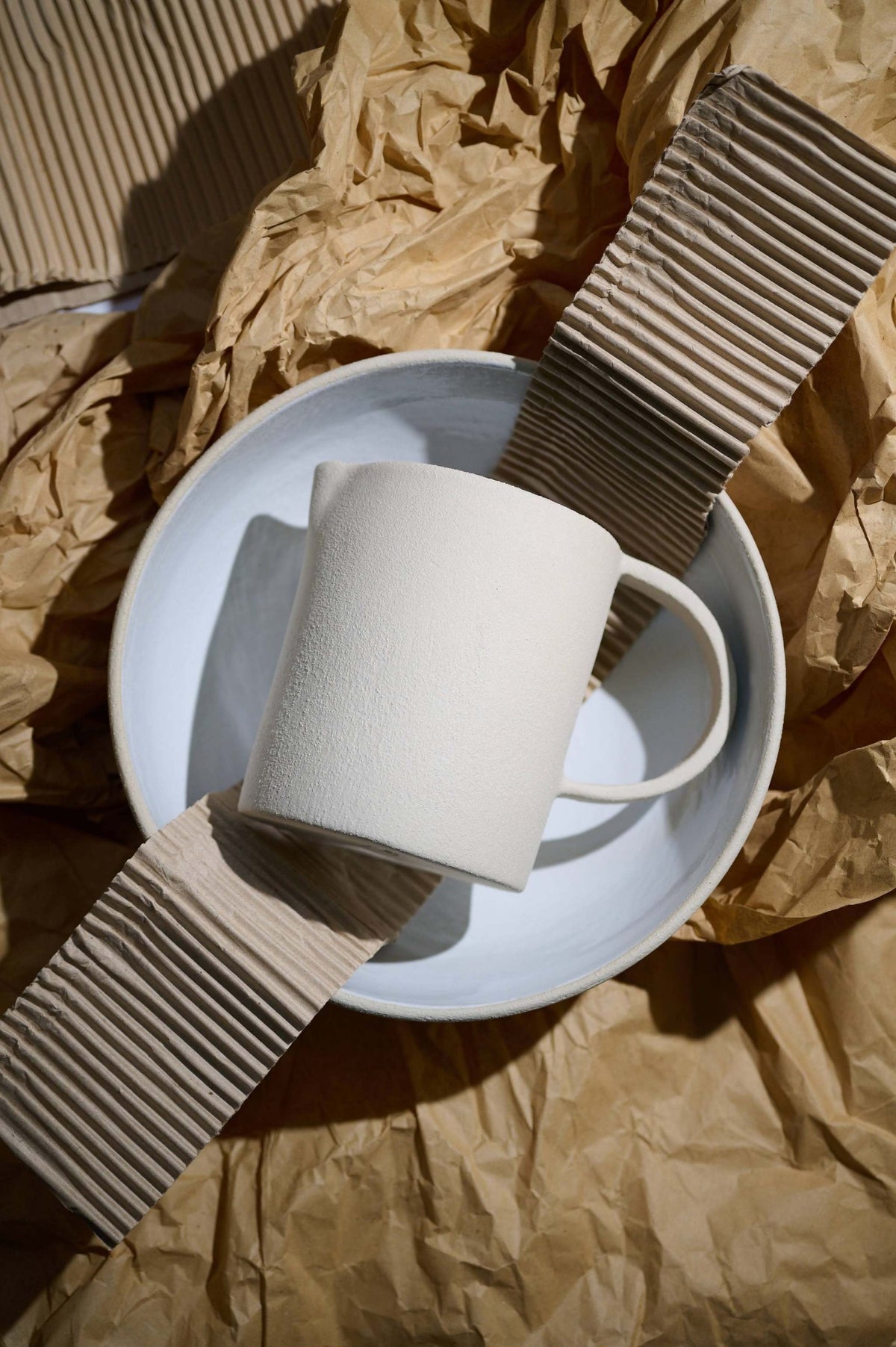Stoneware pitcher resting on a matching plate over brown paper and corrugated card in strong sun