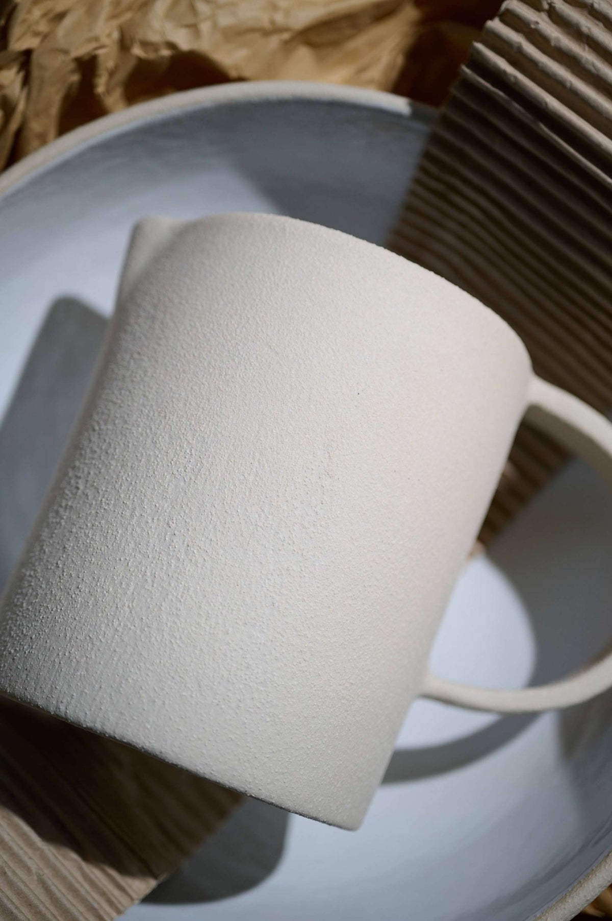 Close detail of the pitcher's unglazed clay surface and handle beside a white plate in sunlight