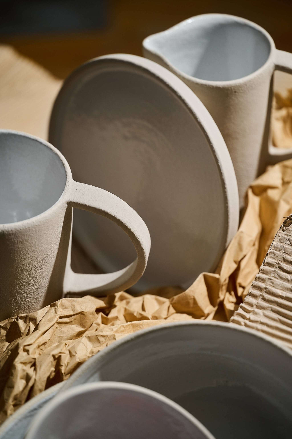 Raw stoneware pitcher grouped with matching bowls and plates in a warm, sunlit table setting
