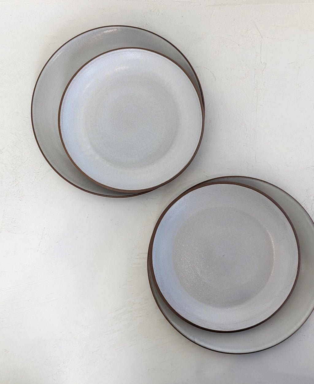 Hand-thrown stoneware coupe dinner plate and salad plate in white glaze, two nested pairs photographed from above