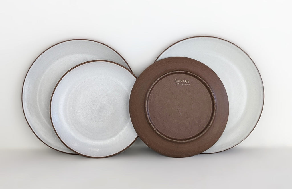 Hand-thrown stoneware coupe plates in white glaze with one turned to show the bare red clay back and maker stamp