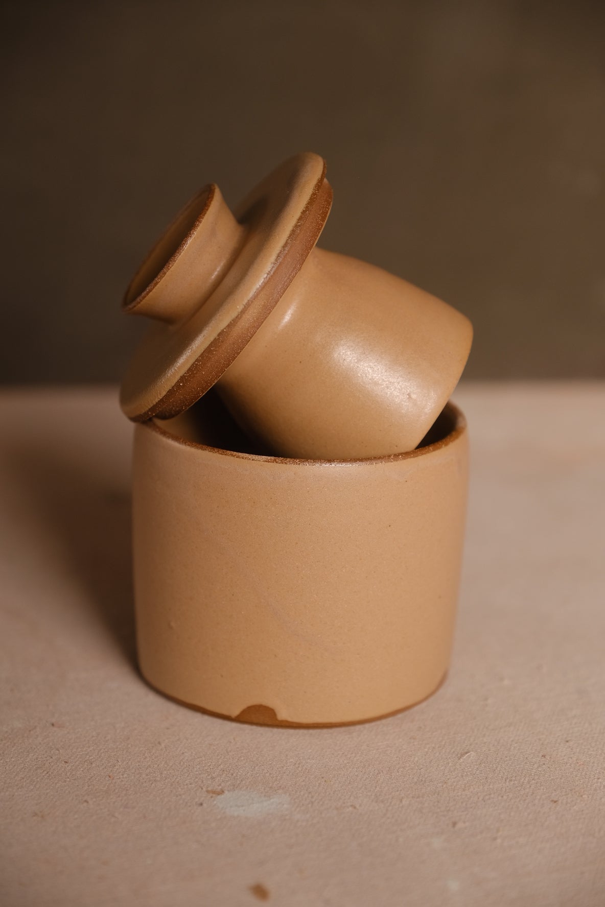 Stoneware French butter keeper in a warm sand glaze with the bell-shaped lid resting at an angle in the crock
