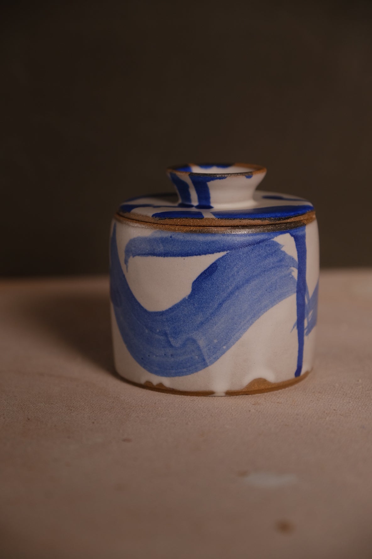 Stoneware French butter keeper with lid on, white glaze with broad cobalt blue brushstrokes, on a clay surface