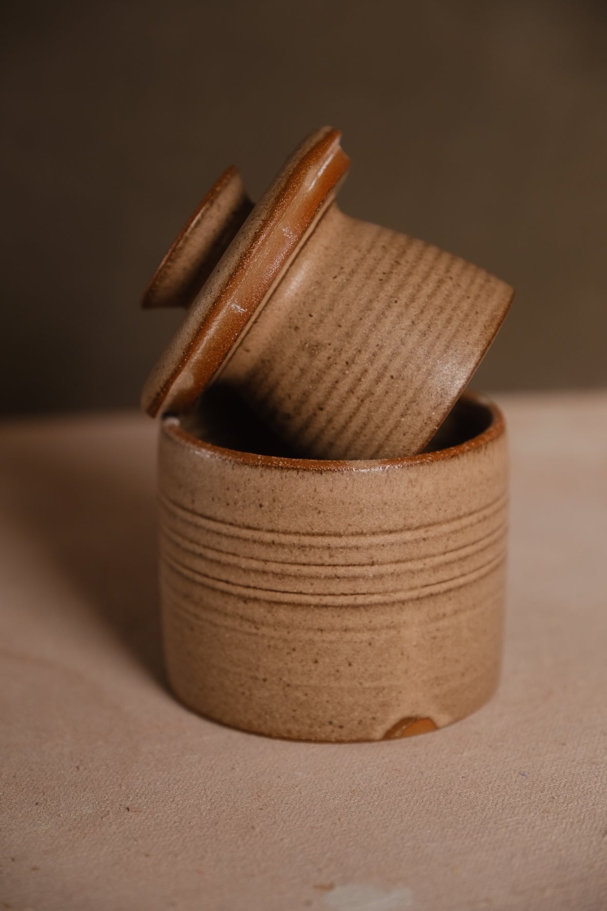 Stoneware French butter keeper in a speckled oatmeal glaze with carved throwing rings, lid tilted in the base