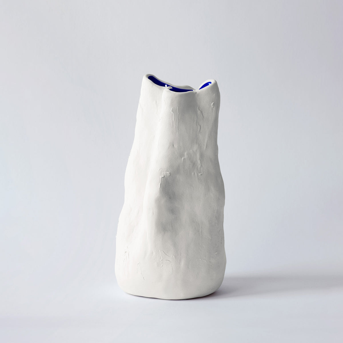 Tall white sculpted porcelain vase with a folded rim standing alone against a soft grey backdrop