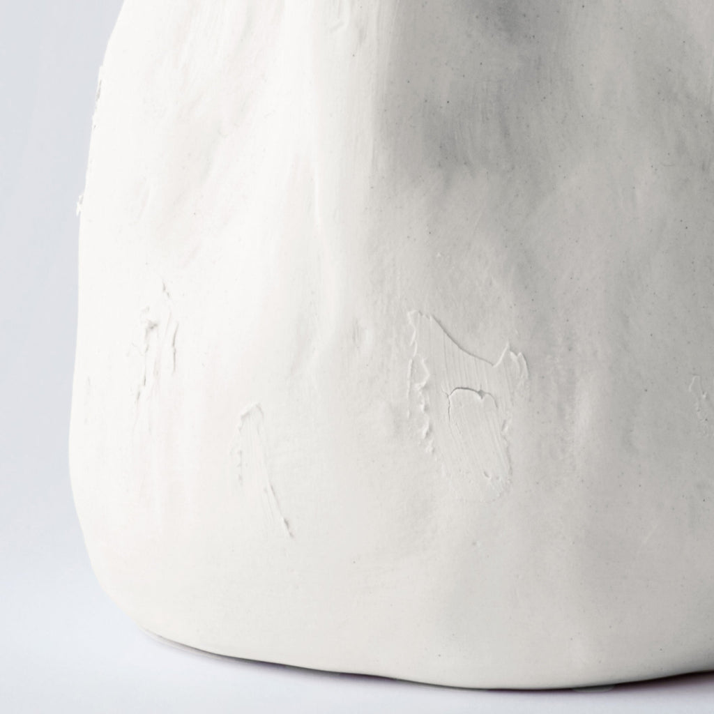 Close detail of the lower half of a tall white sculpted porcelain vase showing its hand-pressed surface