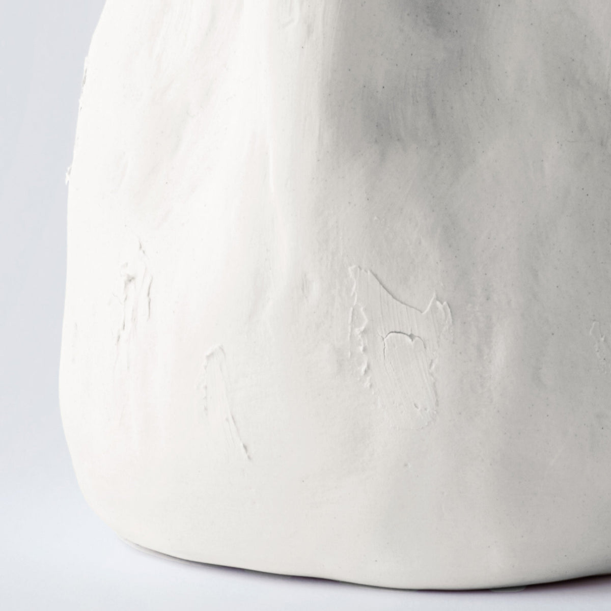 Close detail of the lower half of a tall white sculpted porcelain vase showing its hand-pressed surface