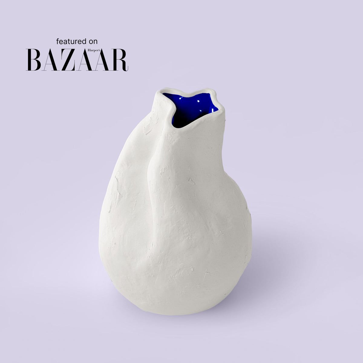 Pear-shaped white sculpted porcelain vase with a pinched neck and cobalt interior on a lavender backdrop