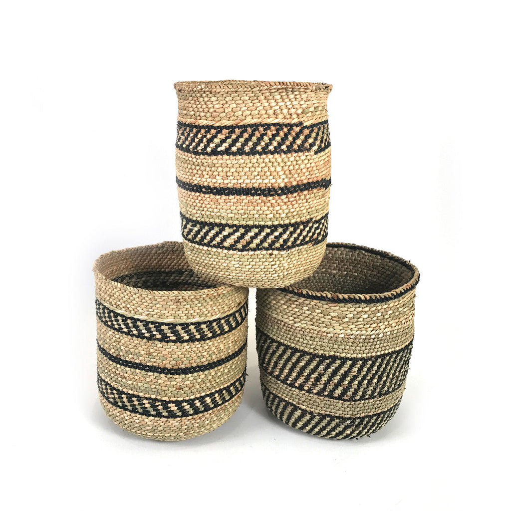 Three handwoven grass baskets stacked in a pyramid, showing natural fiber and black plant-dyed stripes