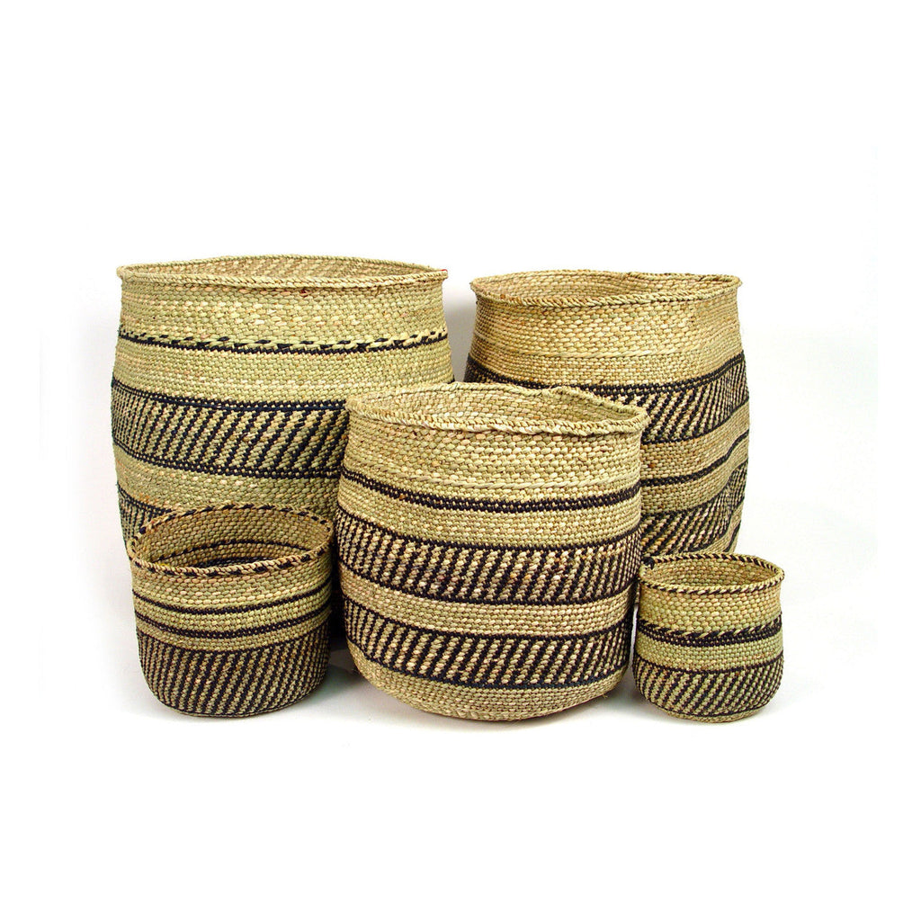 Five handwoven grass baskets in natural and black stripes, nested and stacked in a range of sizes on a white ground