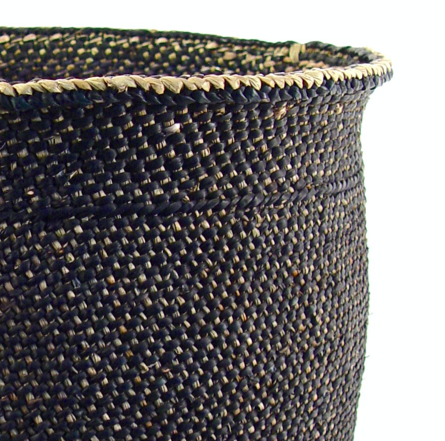 Close-up of a charcoal grass basket's tight weave, with flecks of natural milulu grass and a pale braided rim