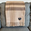 Tan and brown plaid baby alpaca throw hanging flat over the back of a gray sofa, fringe at the hem