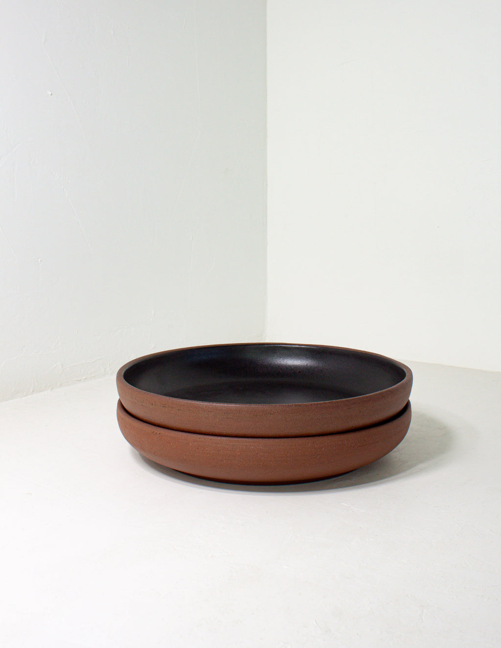 Two black glazed coupe bowls stacked on a gray ground, showing the bare clay outside