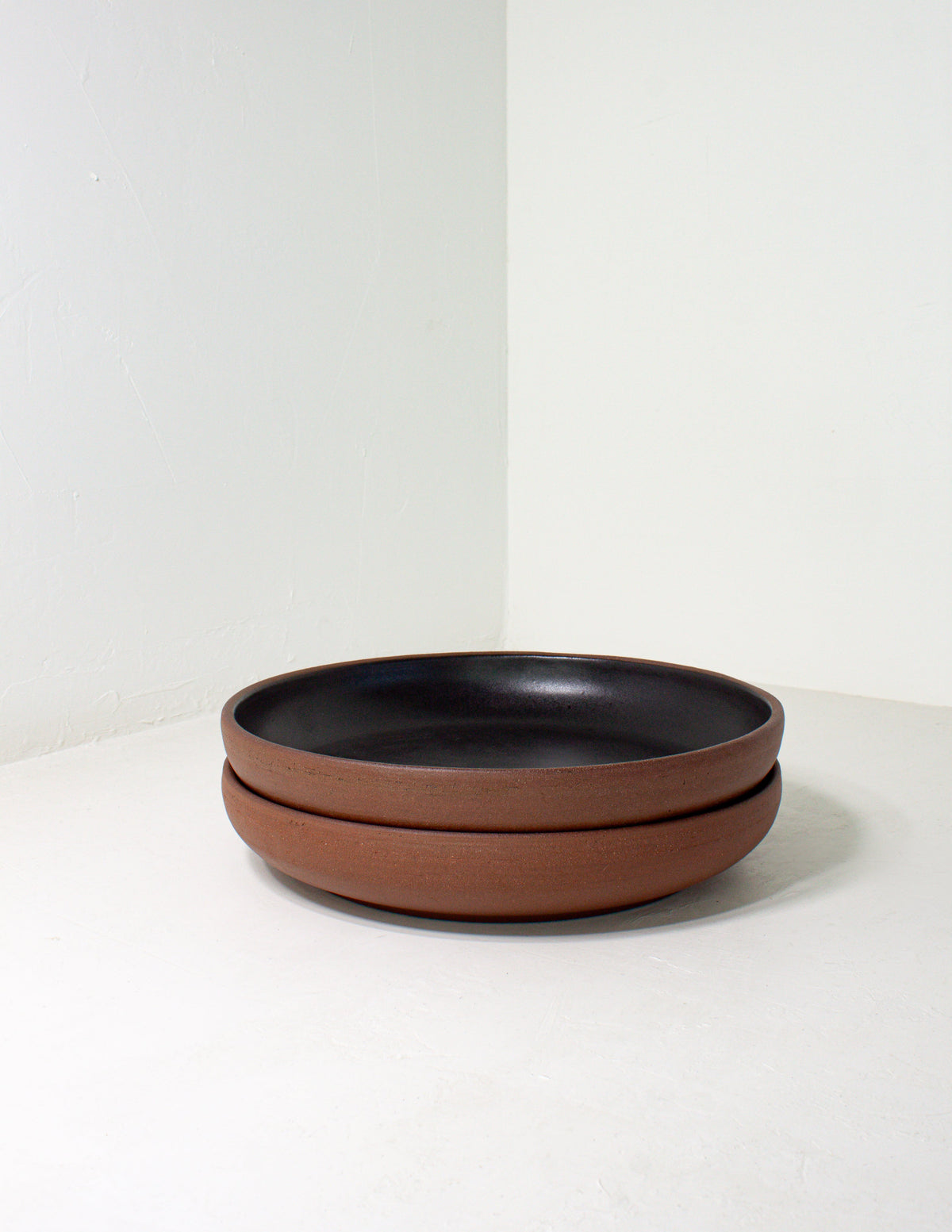 Two black glazed coupe bowls stacked on a gray ground, showing the bare clay outside