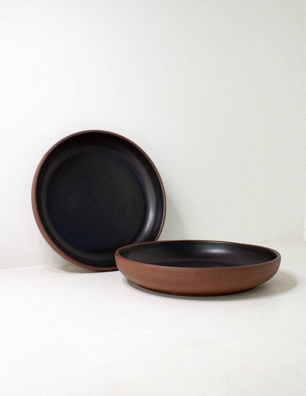Black glazed coupe bowl standing upright with a second bowl lying in front of it