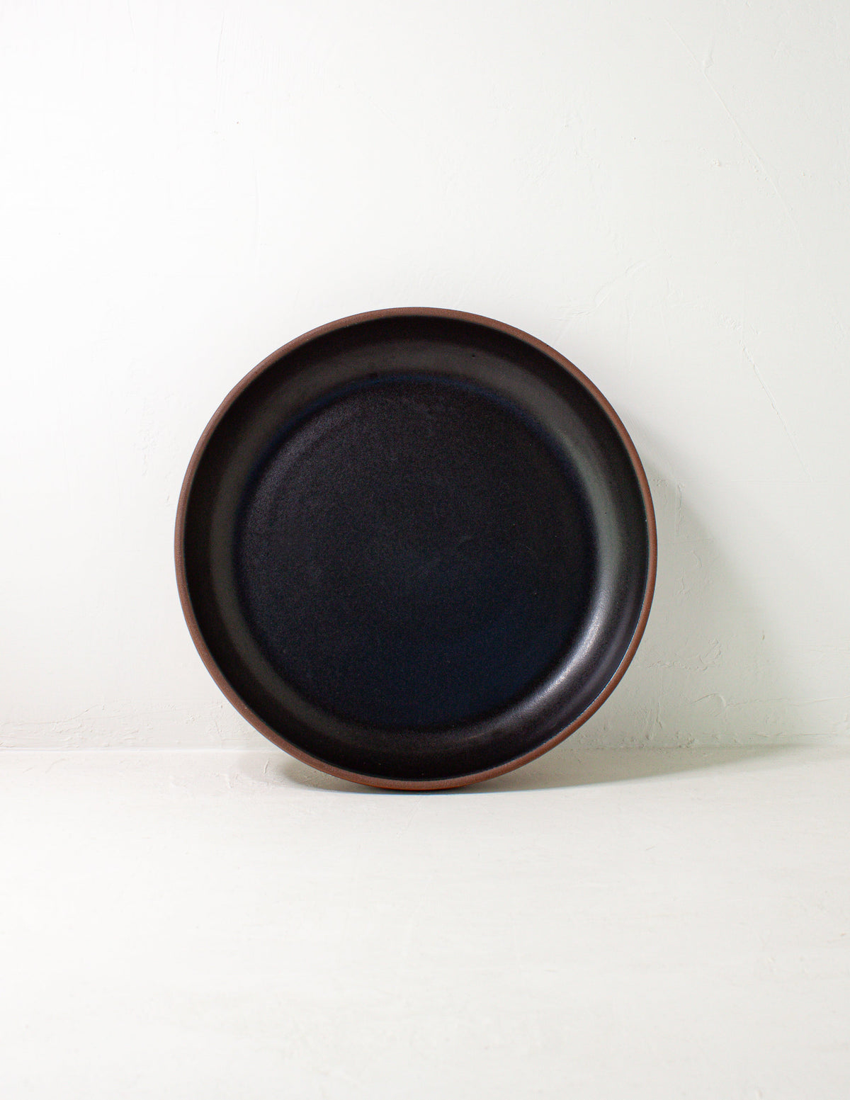 Black glazed coupe serving bowl standing upright on its rim against a pale gray background