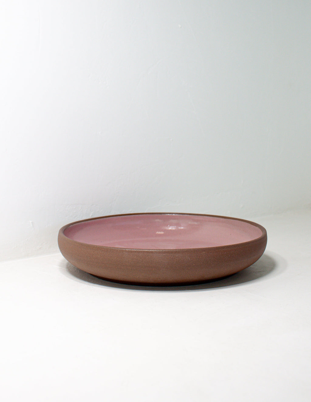 Pink glazed low coupe bowl shown from the side with its bare terracotta clay exterior