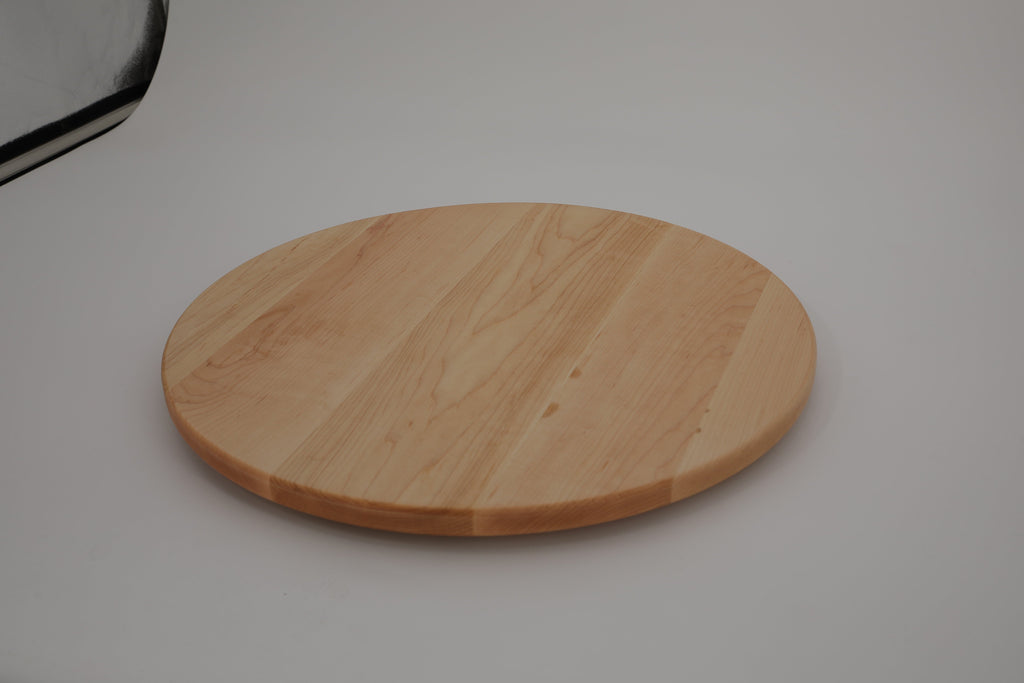 Round maple cutting board on a grey studio surface, low angled view showing the thin edge